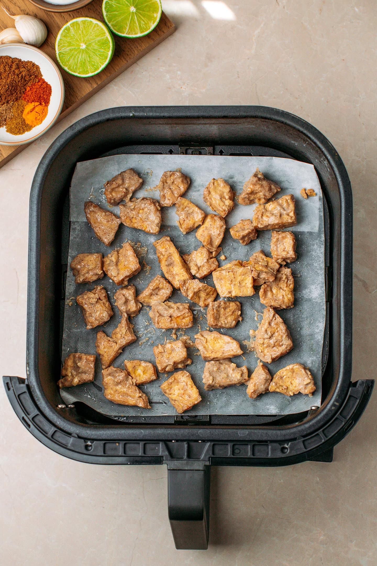 Marinated tofu pieces in an air fryer basket.