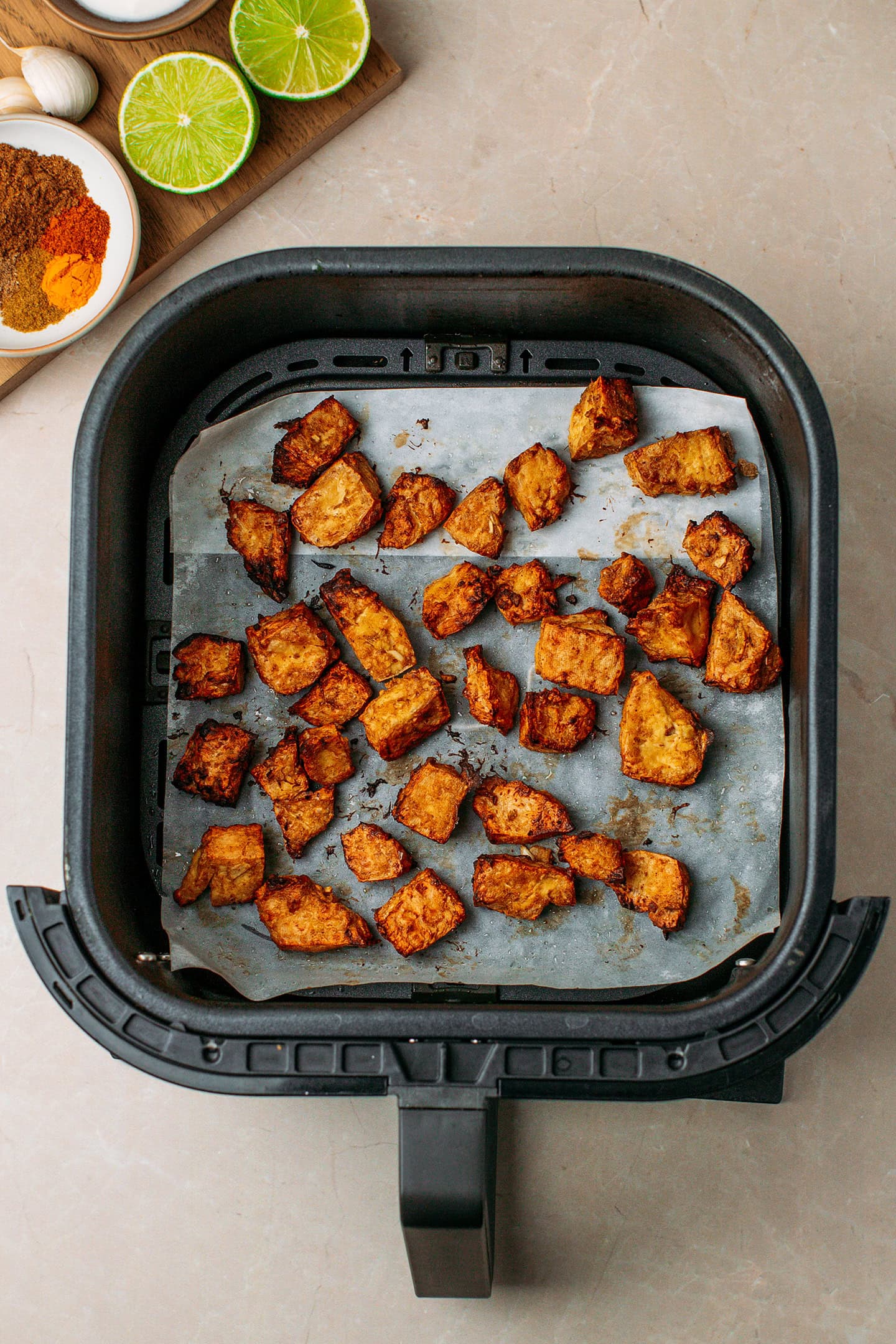 Charred tofu pieces in an air fryer basket.