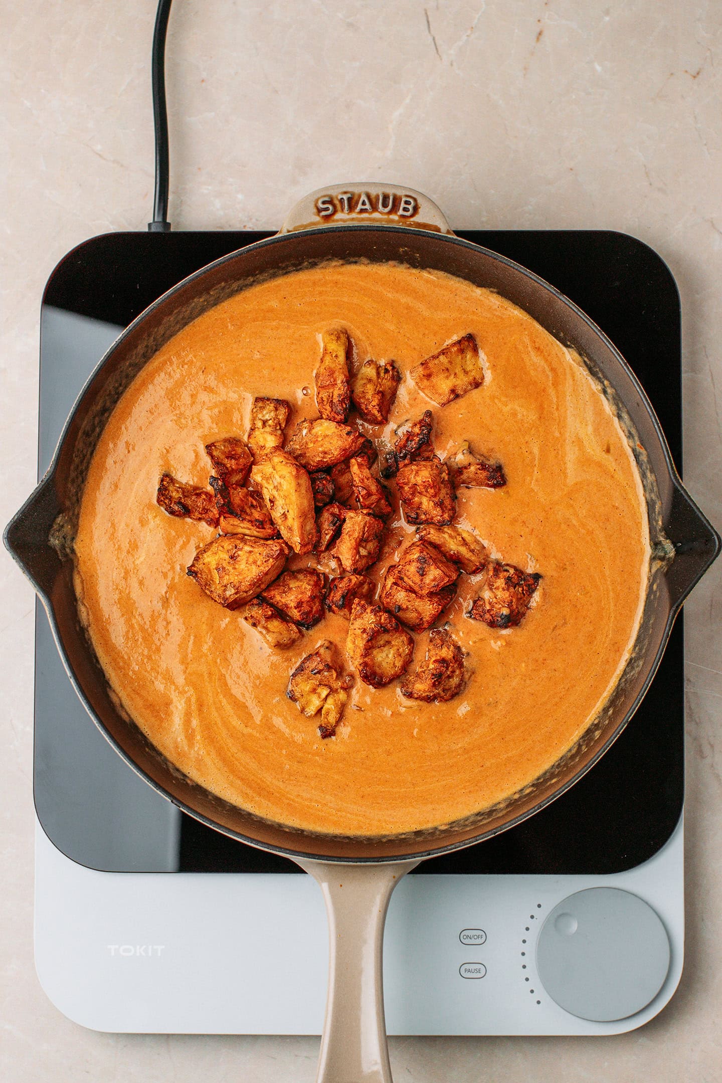 Curry sauce and charred tofu pieces in a skillet.
