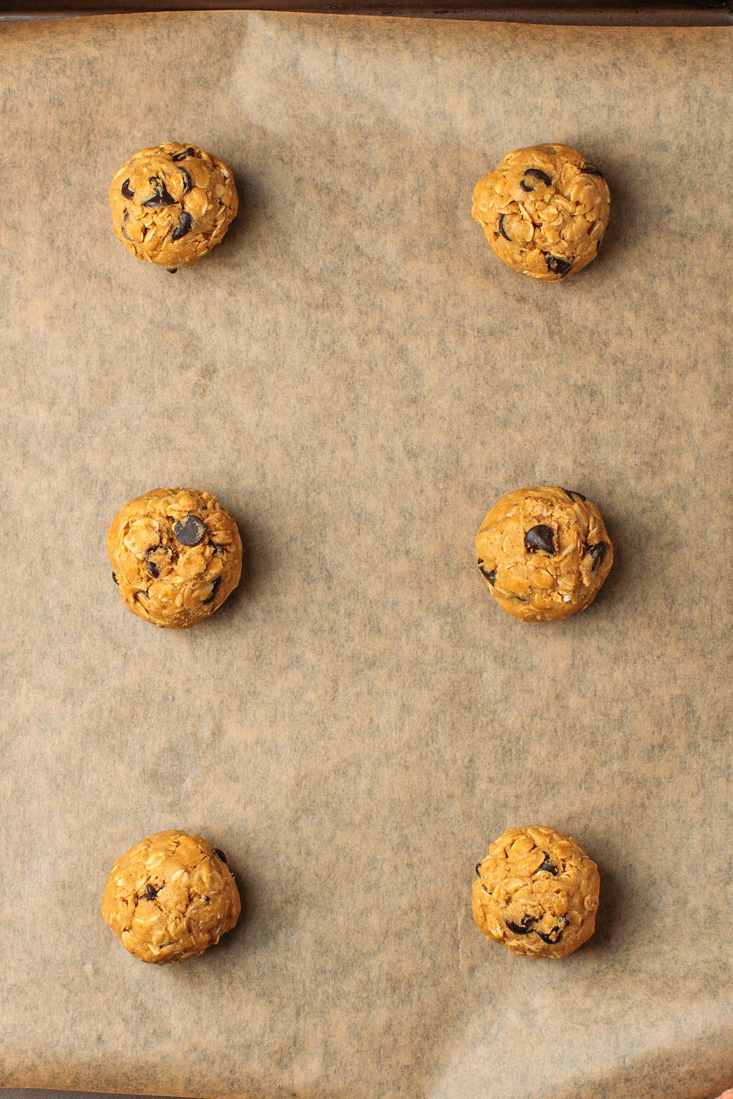 Six cooke dough balls on a baking sheet.