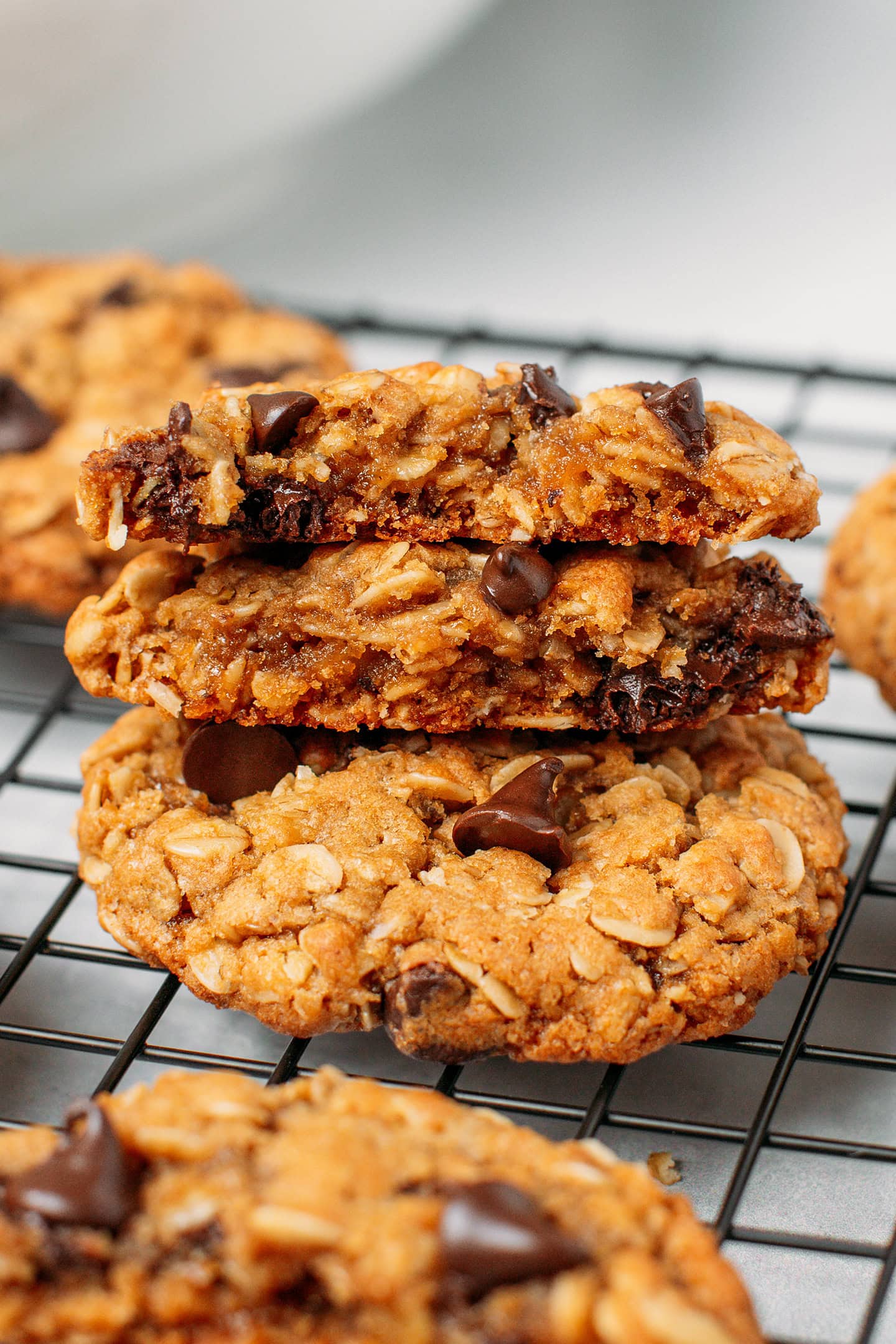 Three oatmeal chocolate chip cookies stacked on a cooling rack.