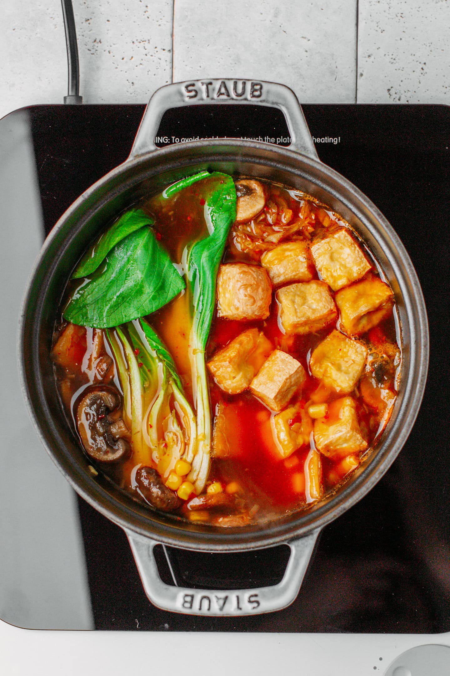 Kimchi broth, pak choy, mushrooms, and tofu in a pot.