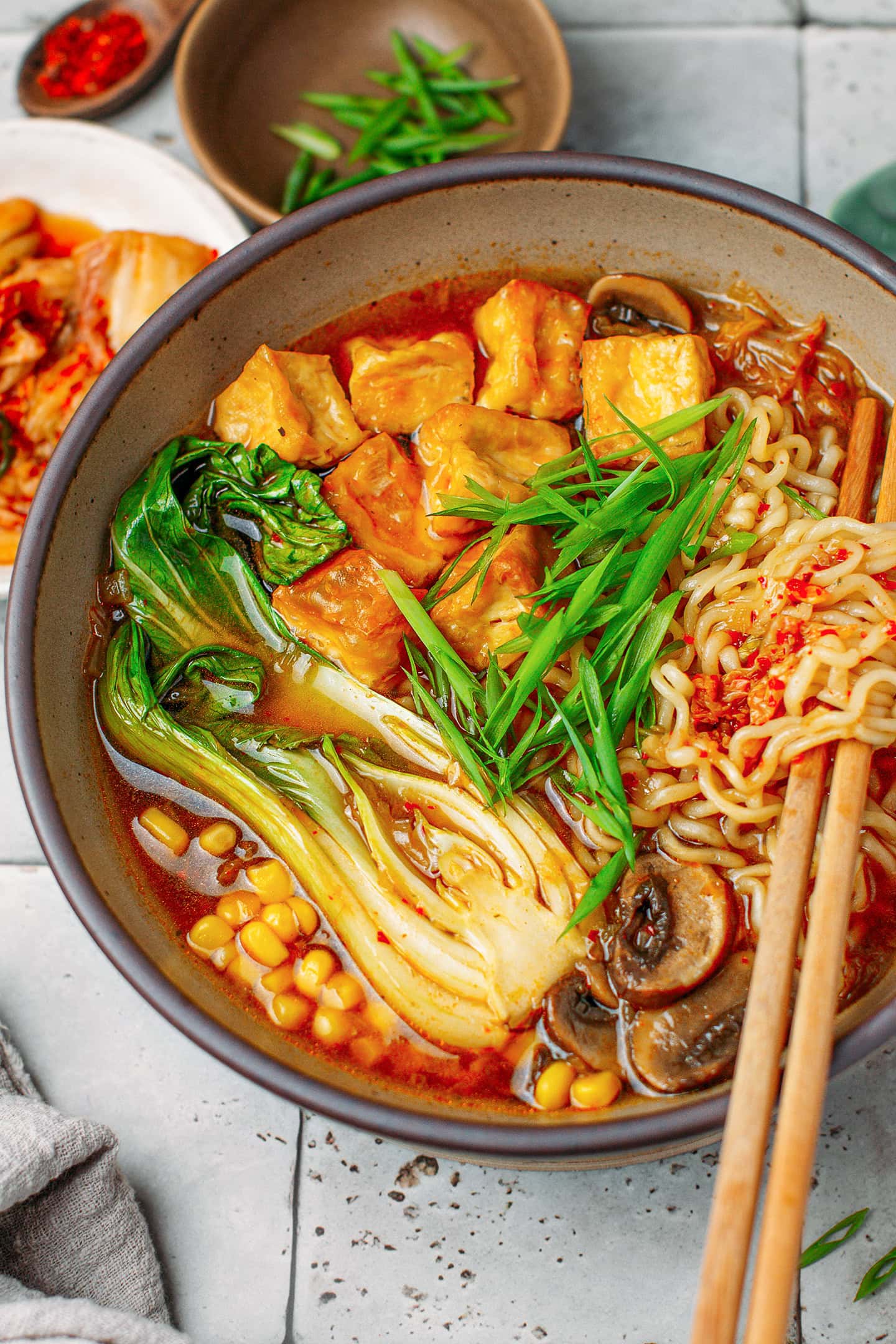 Close-up of kimchi ramen with pak choy, instant noodles, tofu, and mushrooms.