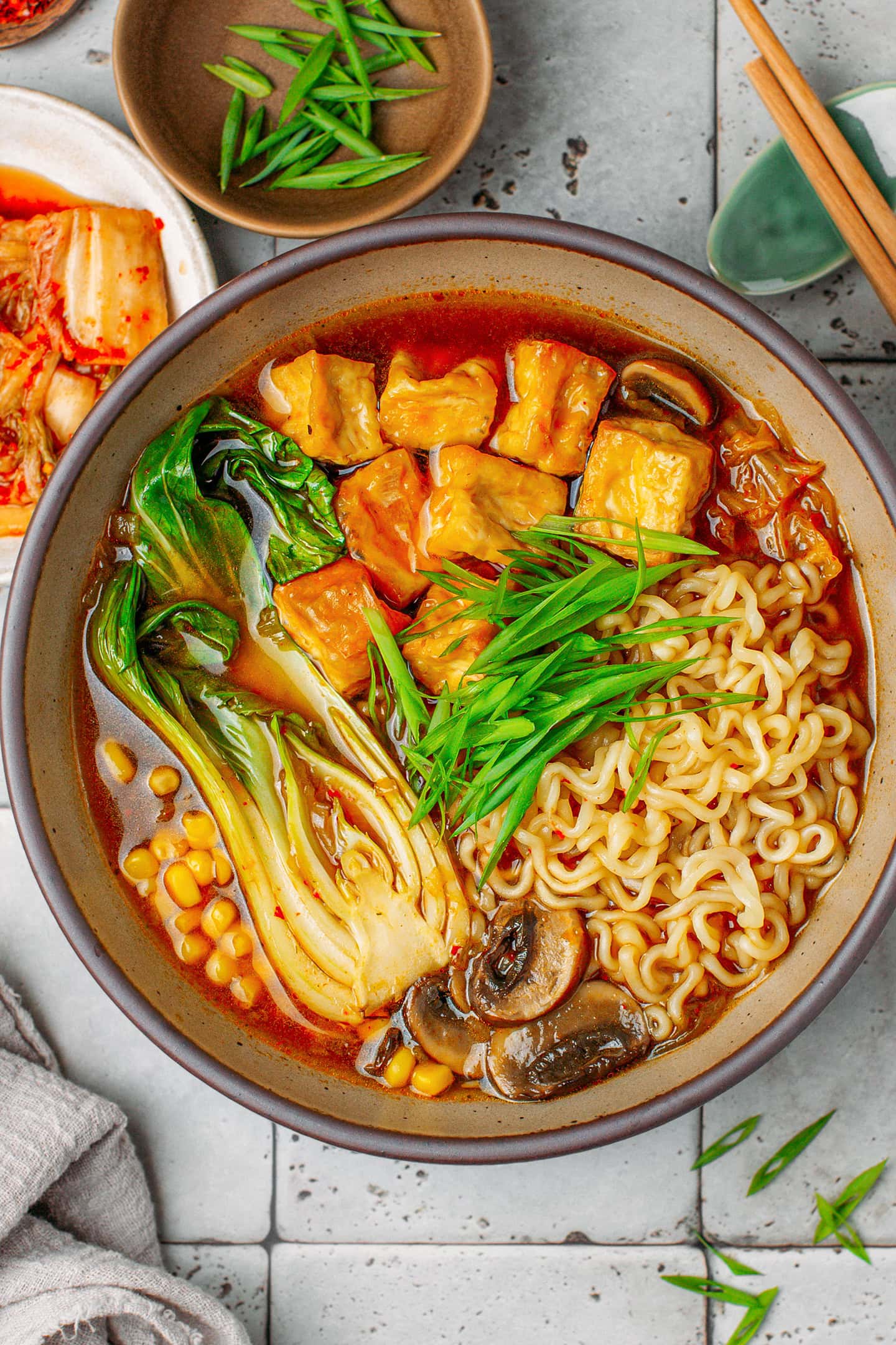 Bowl of kimchi ramen with instant noodles, pak choy, tofu, mushrooms, and chopped green onions.