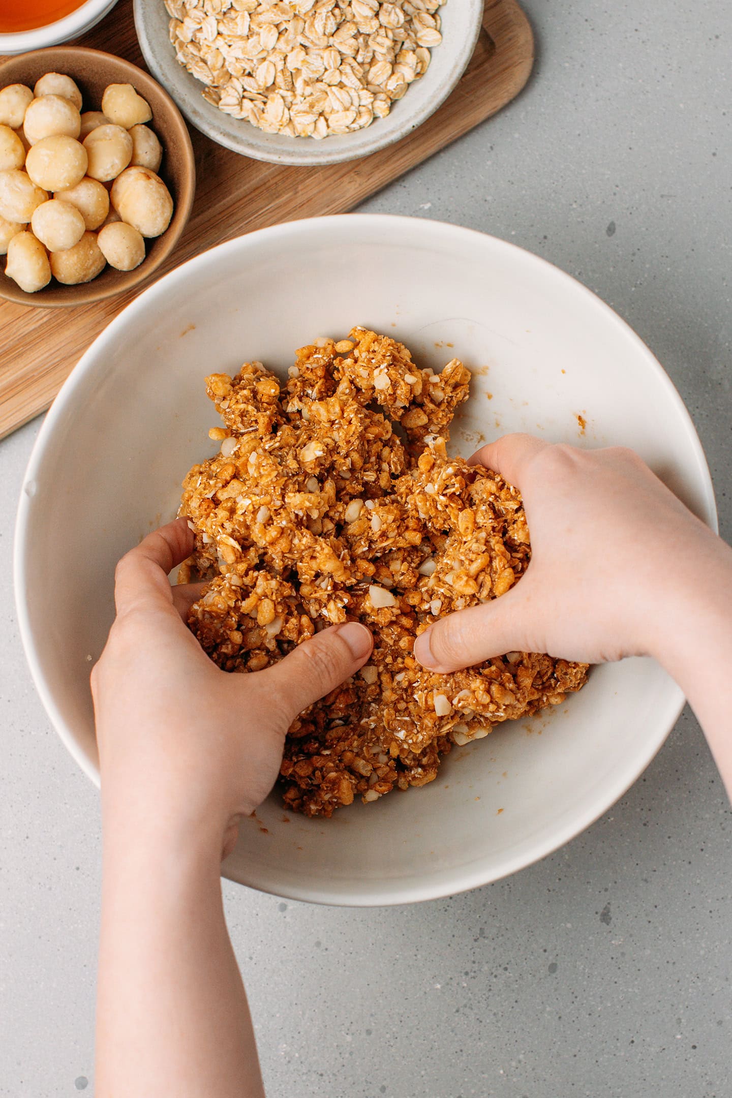 Using hands to mix a sticky granola bar mixture inside a mixing bowl.