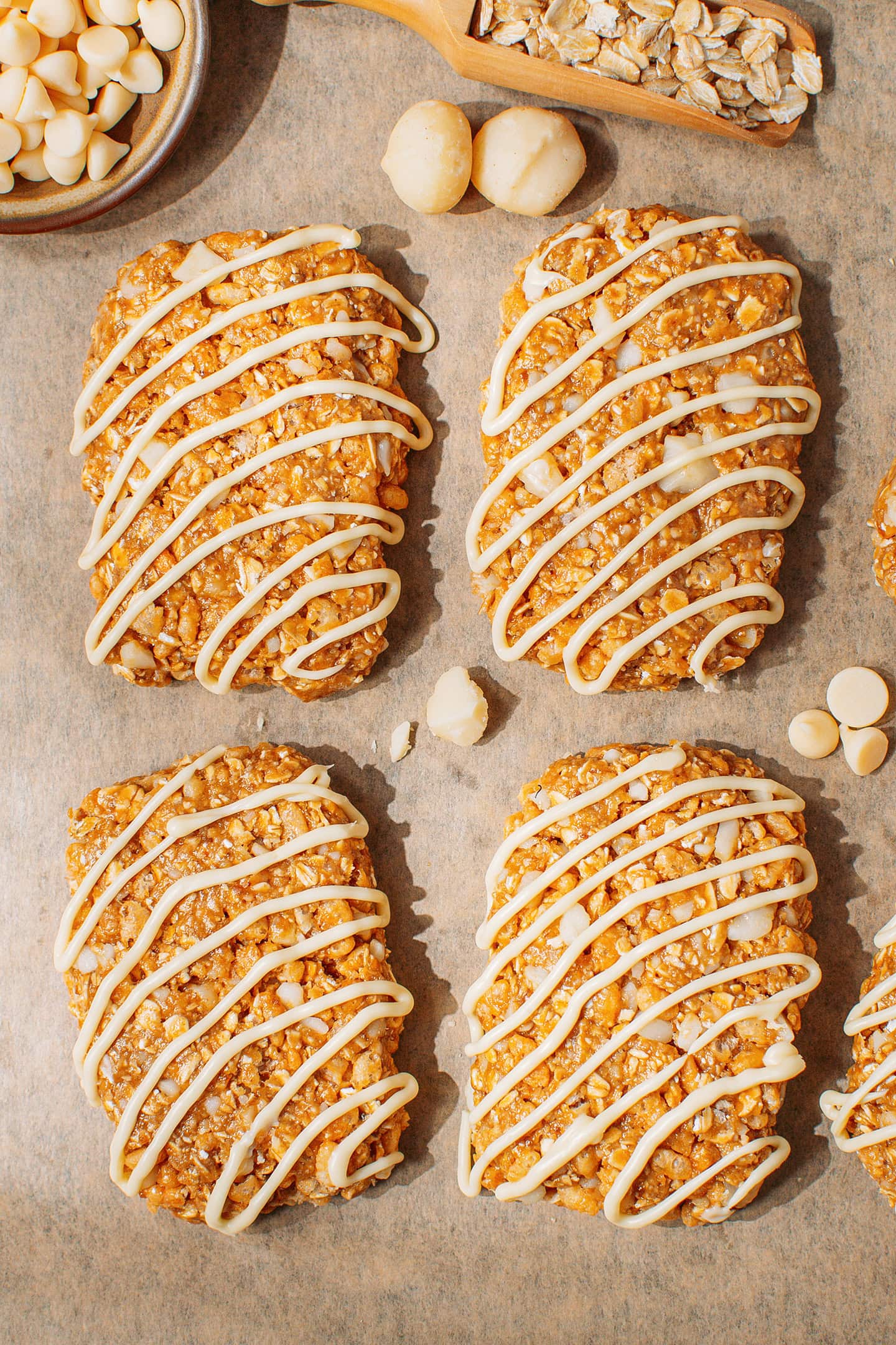 Four macadamia nut granola bars drizzled with vegan white chocolate on a baking sheet.