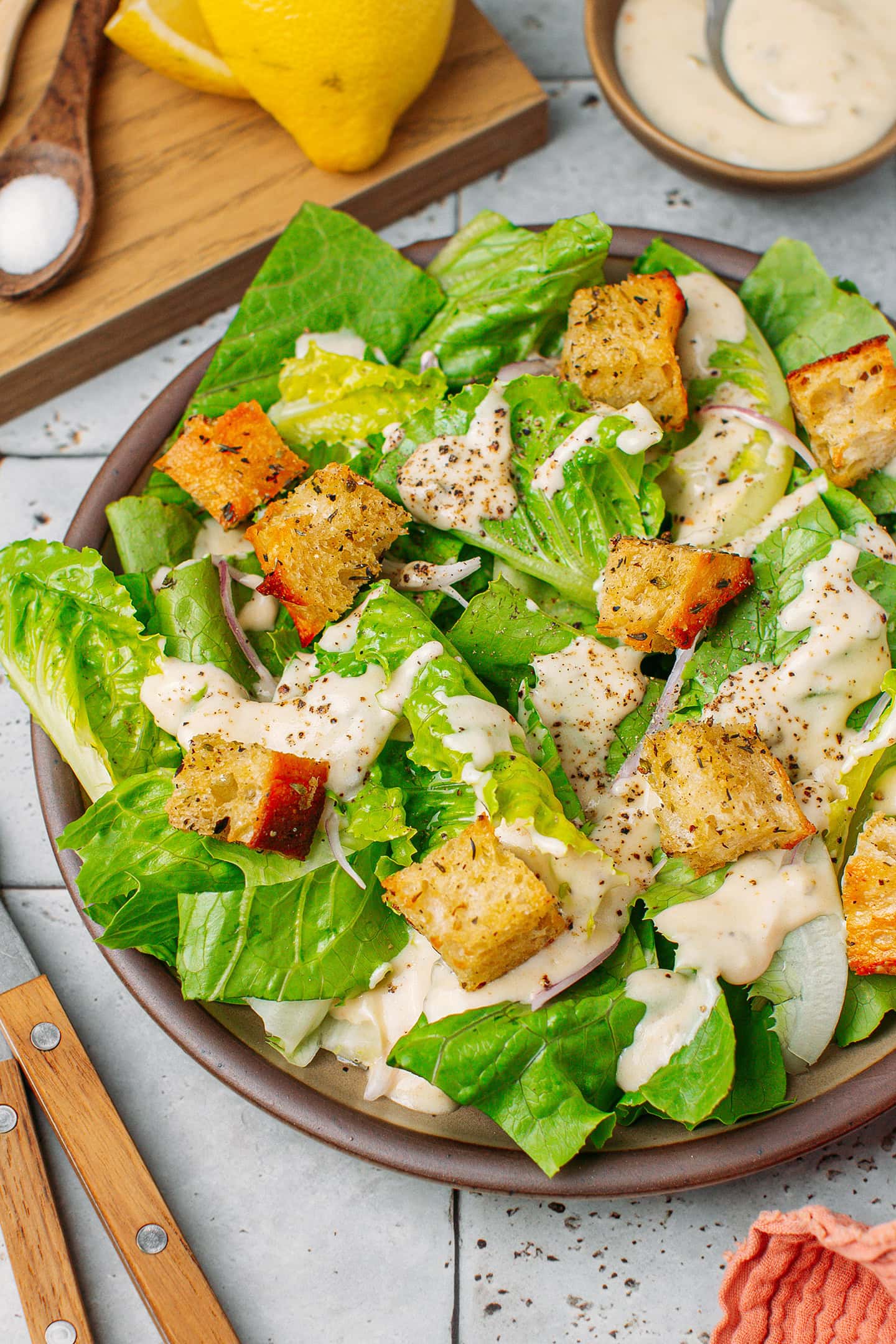 Close-up of Caesar salad with a creamy dressing, croutons, and sliced shallots.
