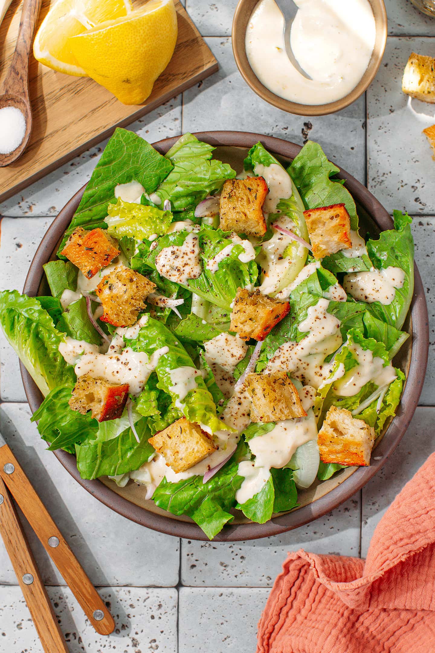 Vegan Caesar salad with croutons, ground black pepper, and sliced shallots in a serving plate.