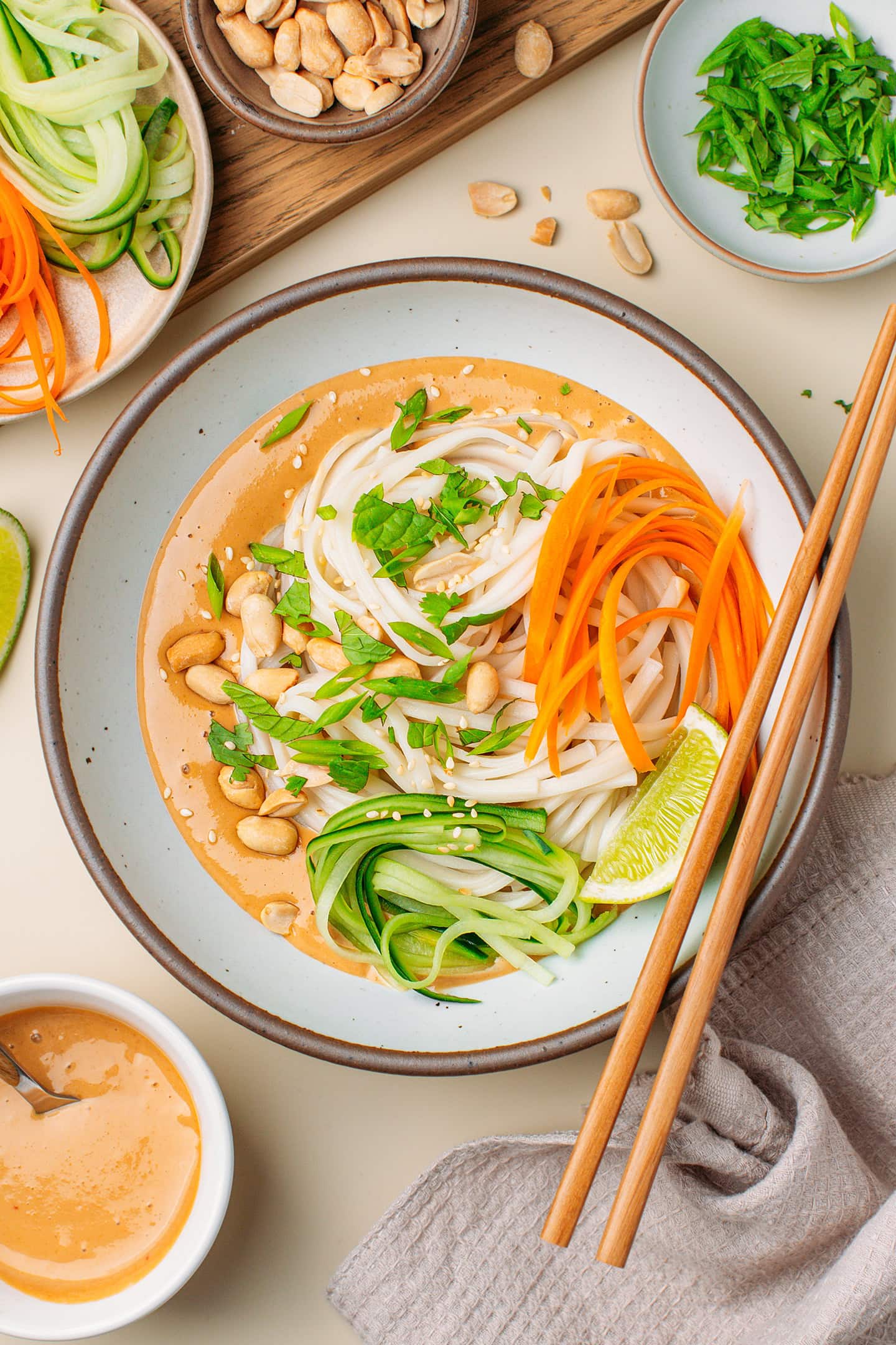 Bowl filled with peanut sauce, noodles, julienned cucumber, carrots, and fresh herbs.