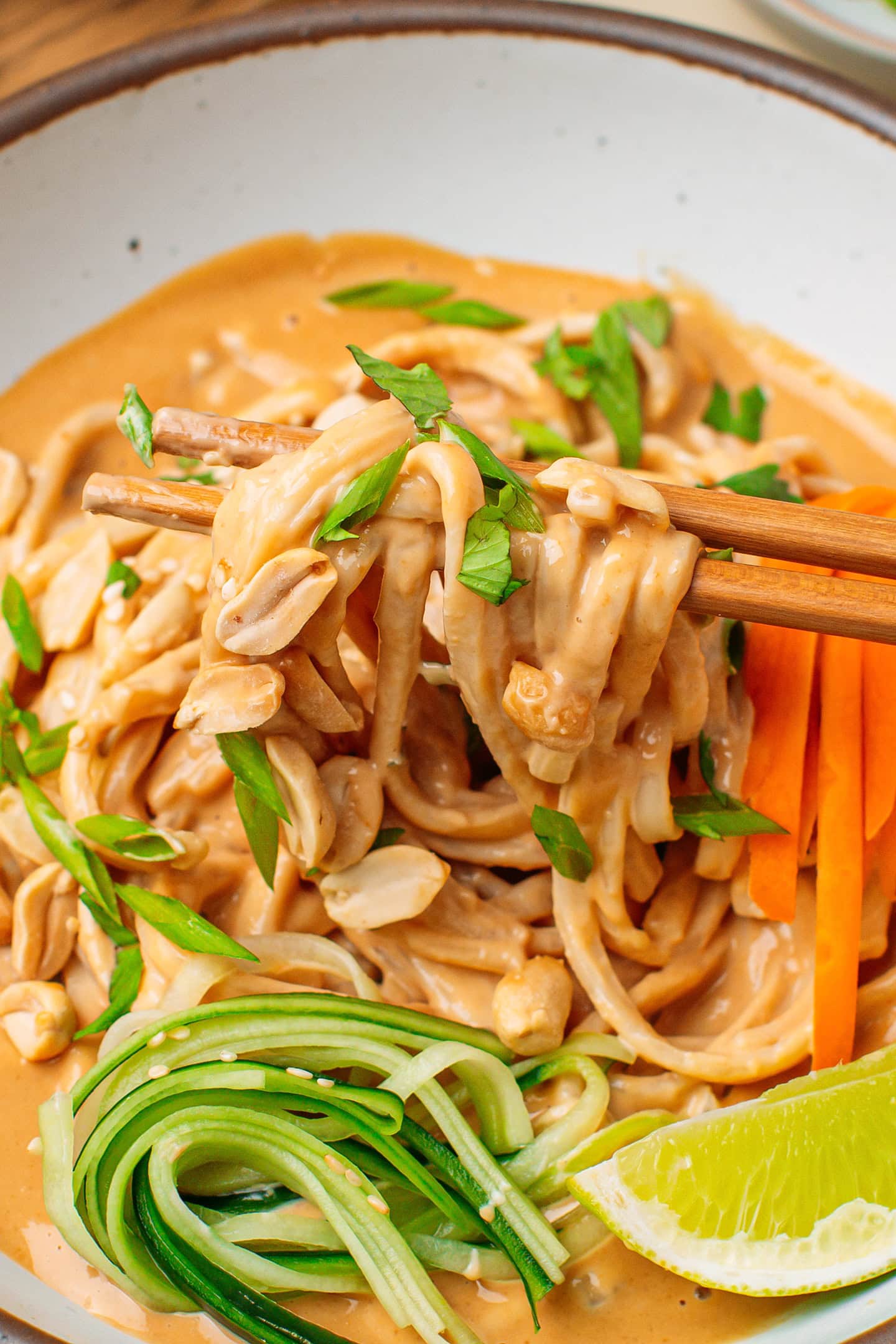 Close-up of peanut noodles held with chopsticks.
