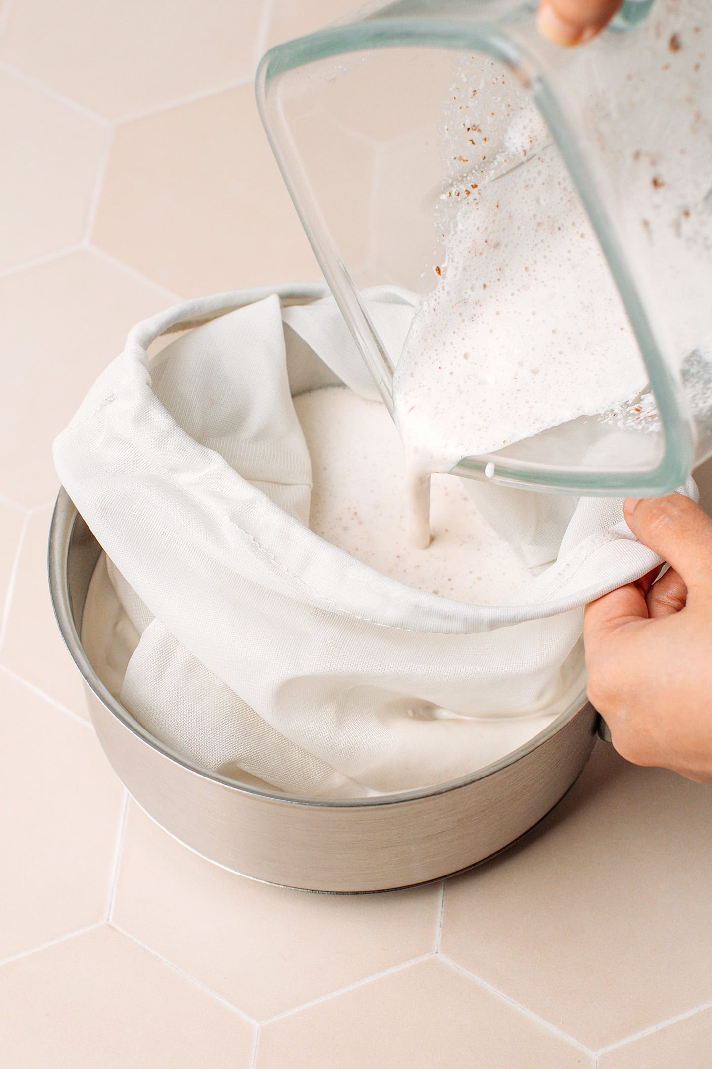 Pouring unfiltered almond and cashew milk into a nut milk bag.