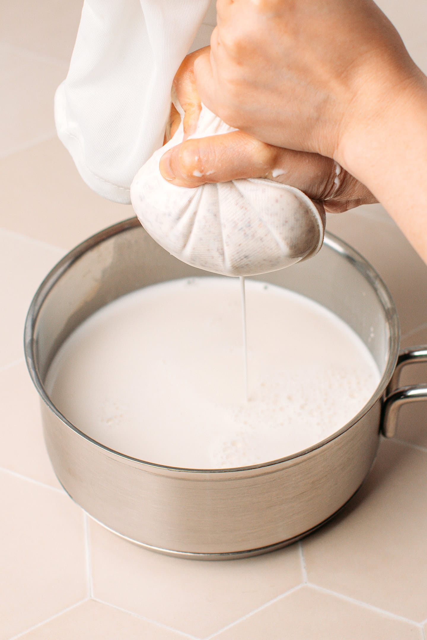 Squeezing a nut milk bag over a saucepan.