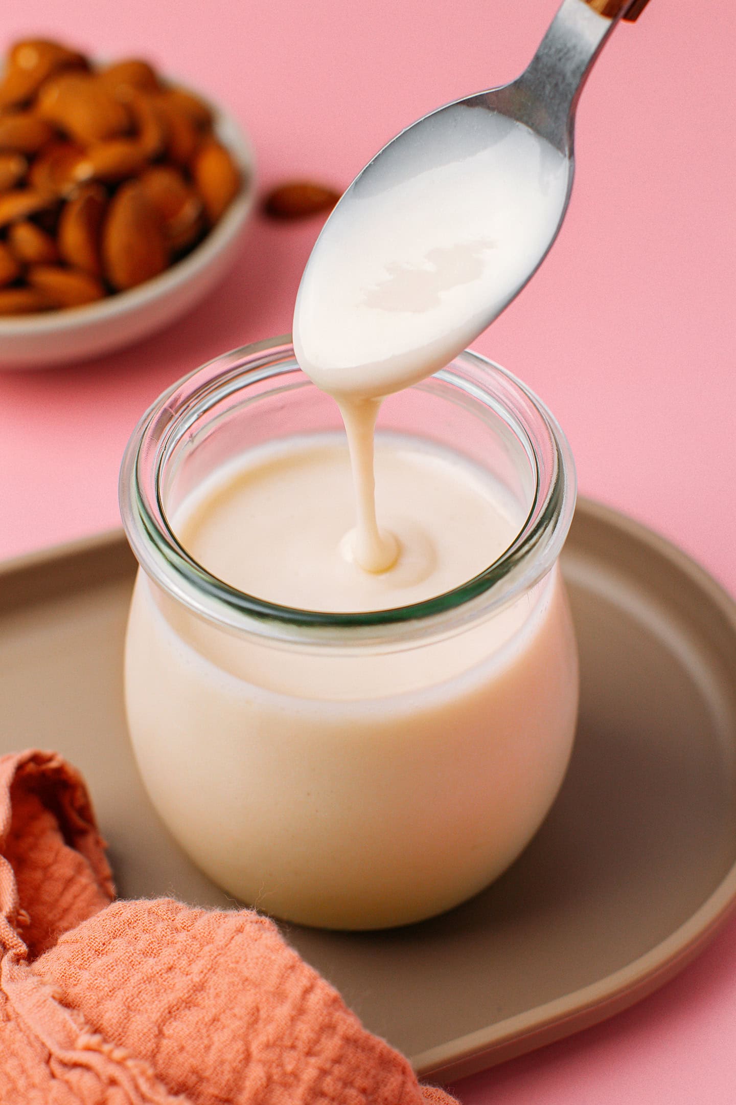 Vegan condensed milk pouring from a spoon into a glass jar.