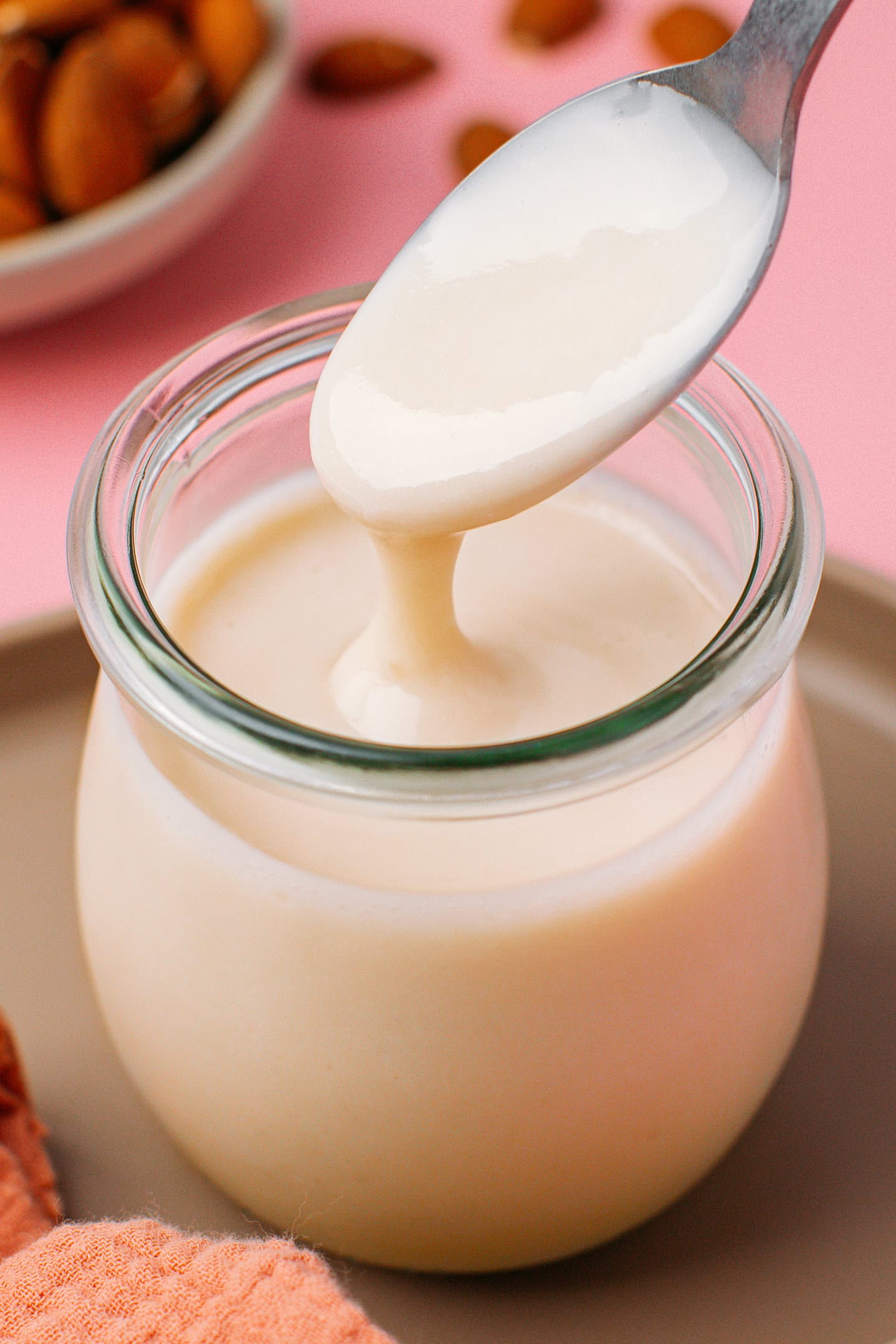 Vegan condensed milk pouring from a spoon into a glass jar.