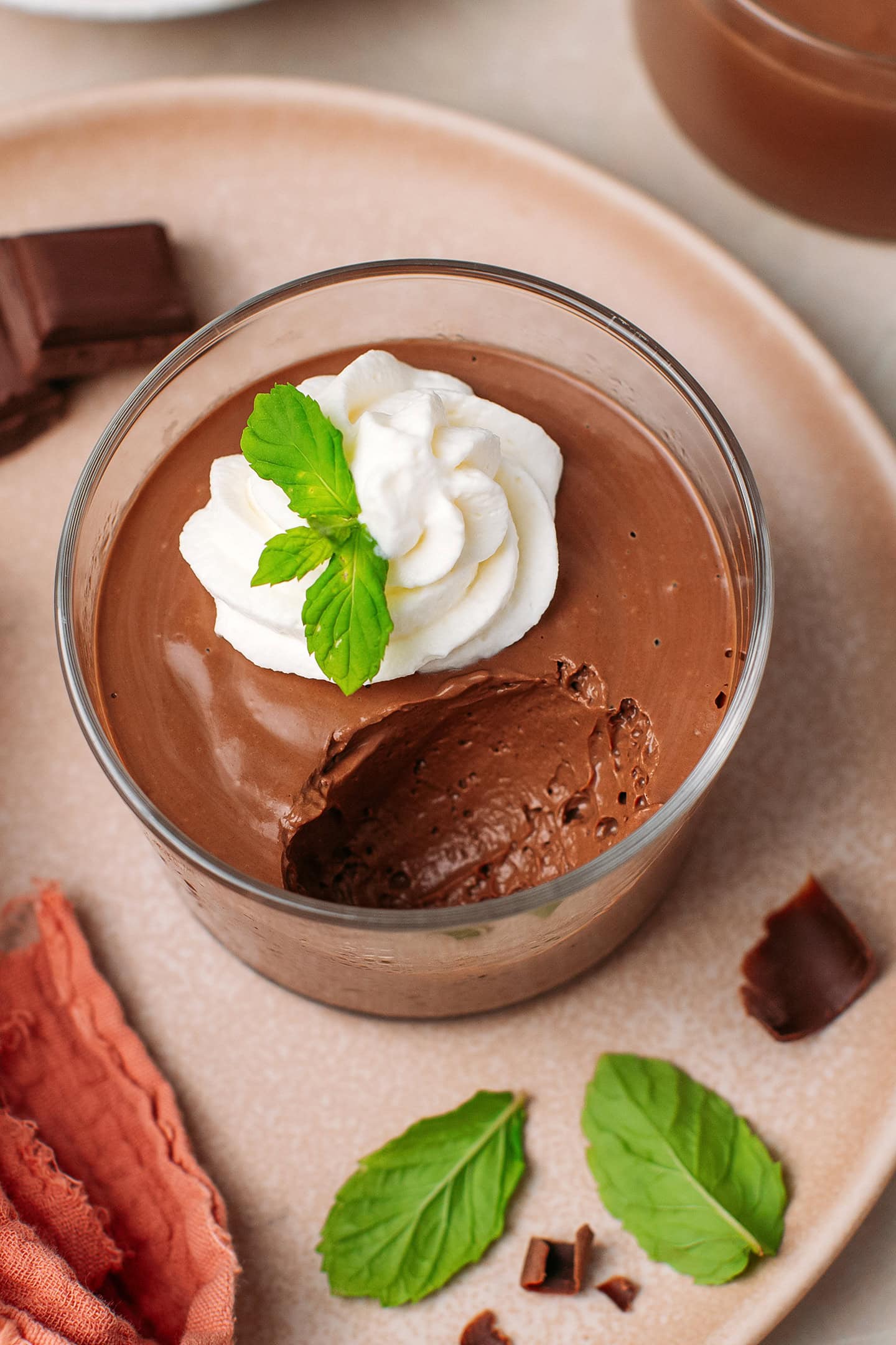 Tofu chocolate mousse in a ramekin, garnished with vegan whipping cream and mint leaves.