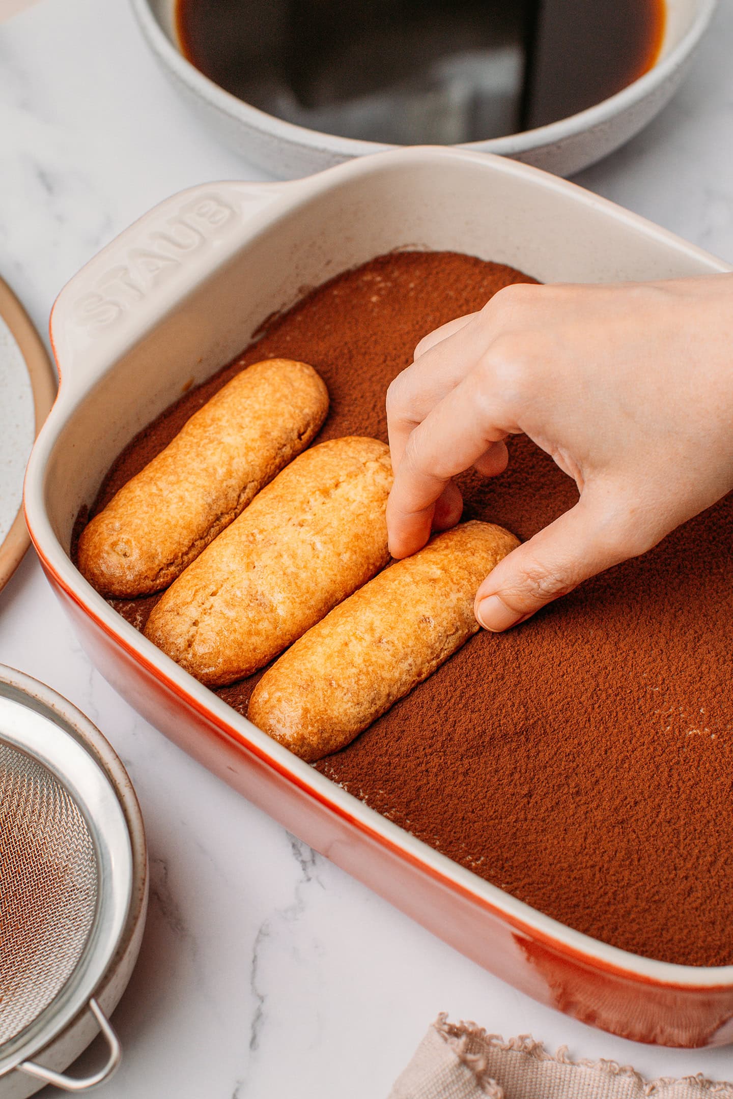 Arranging a ladyfinger over a layer of cream inside a baking dish.