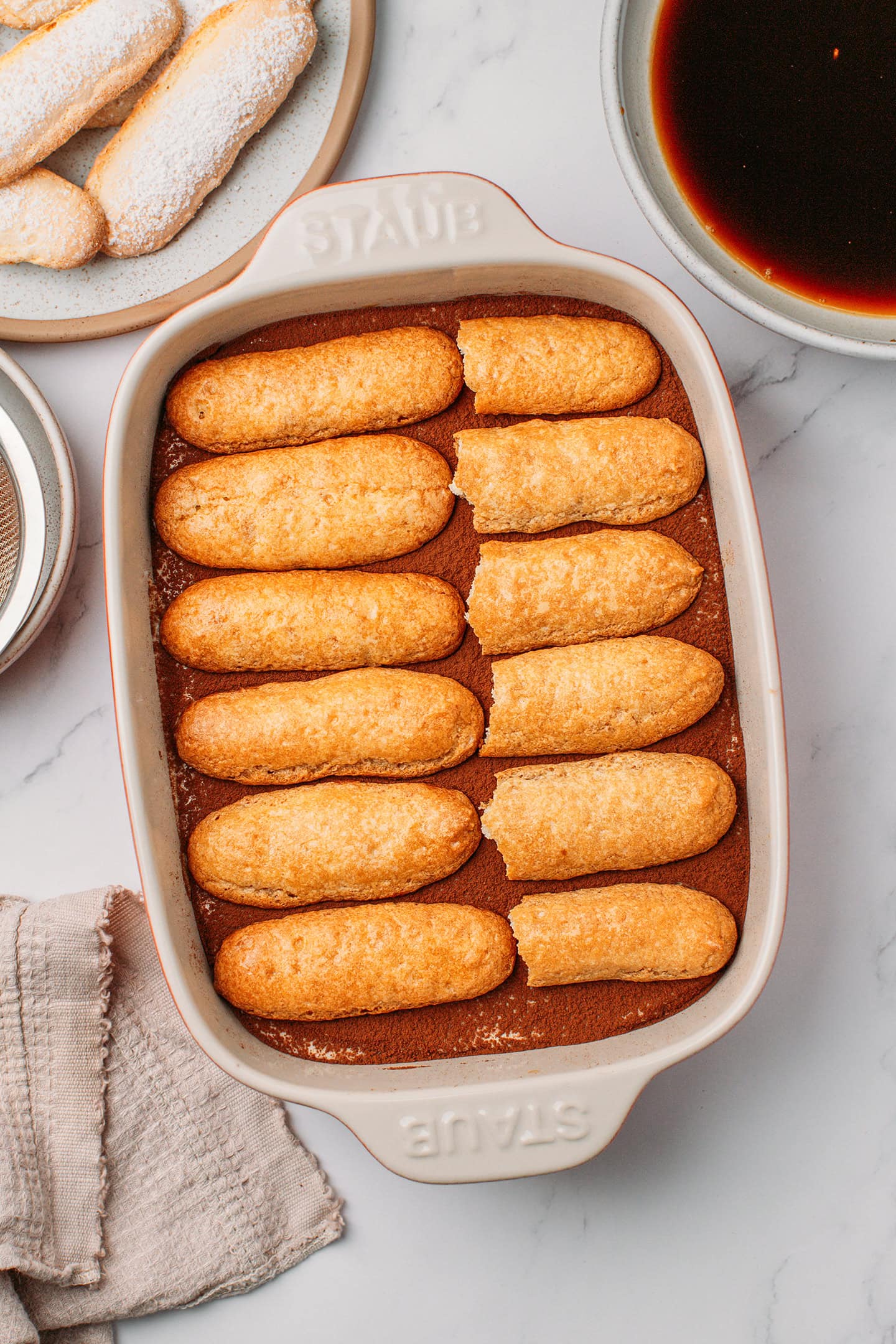 Ladyfingers placed over vanilla cream inside a baking dish.