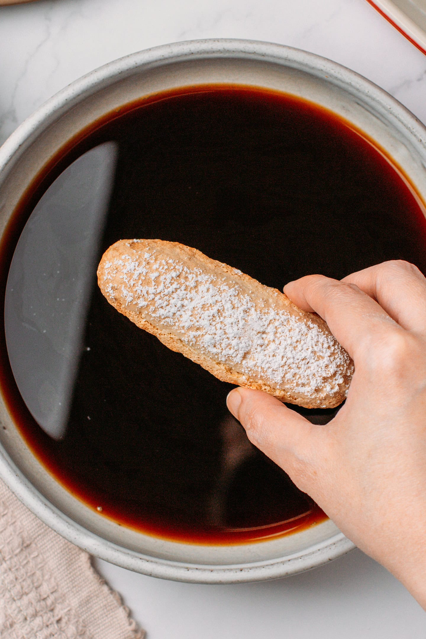 Holding a ladyfinger over a bowl of espresso.