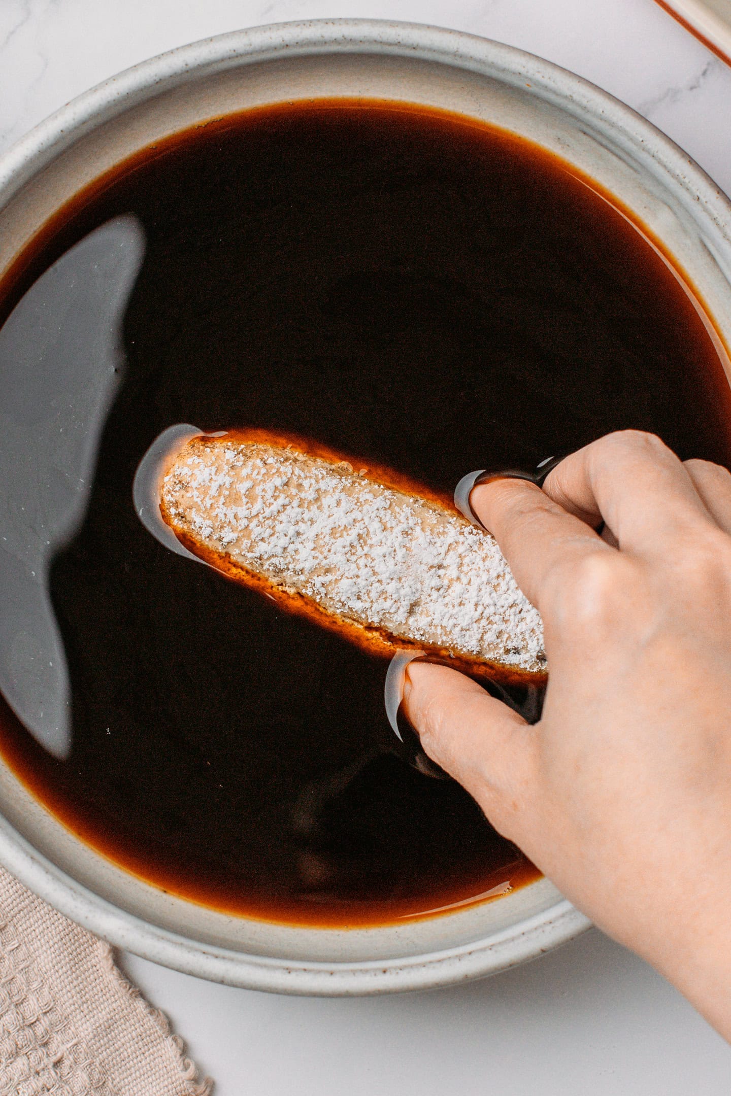 Dipping a ladyfingers into a bowl of espresso.
