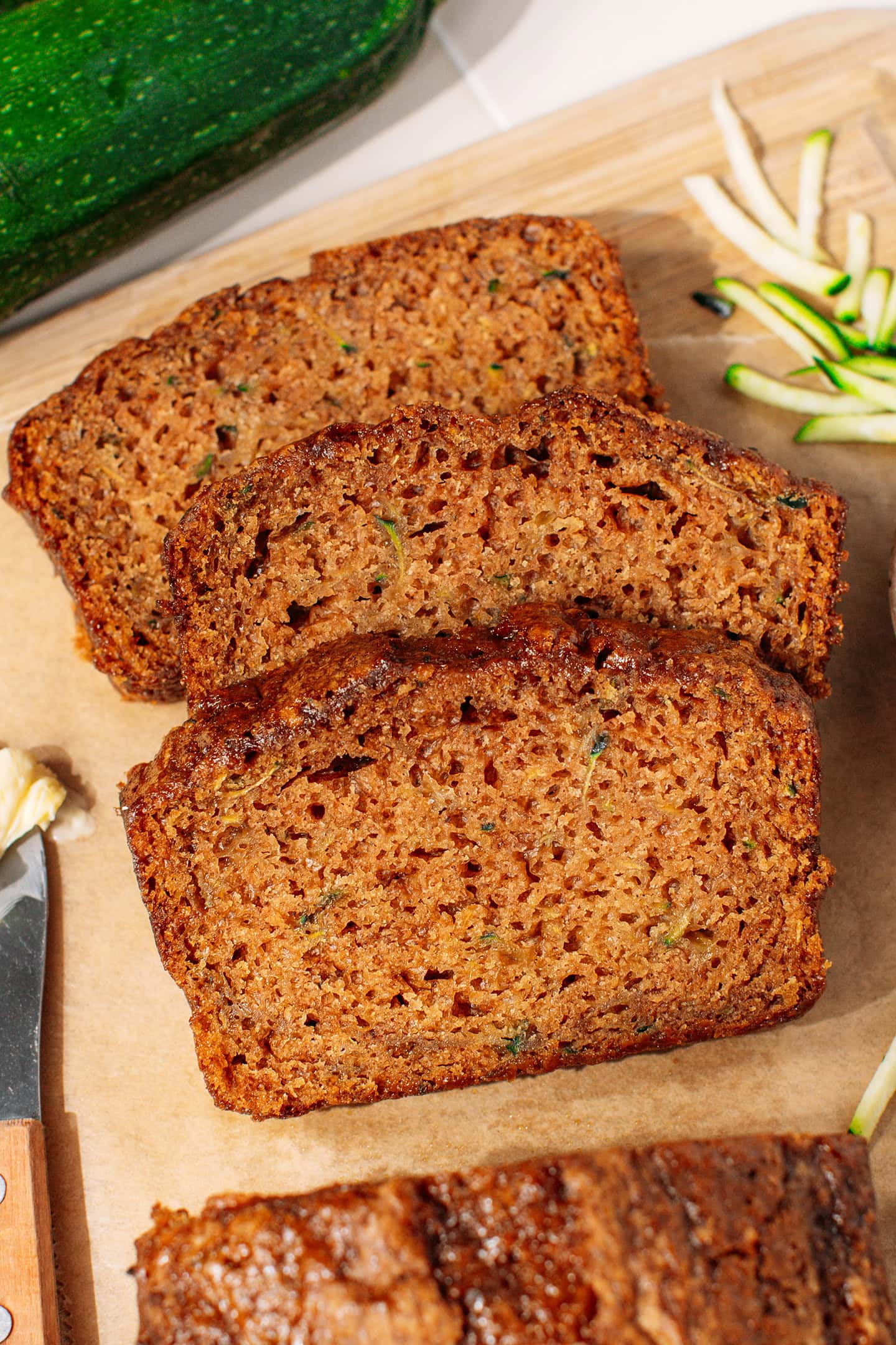 Three slices of vegan zucchini bread on a wooden cutting board.