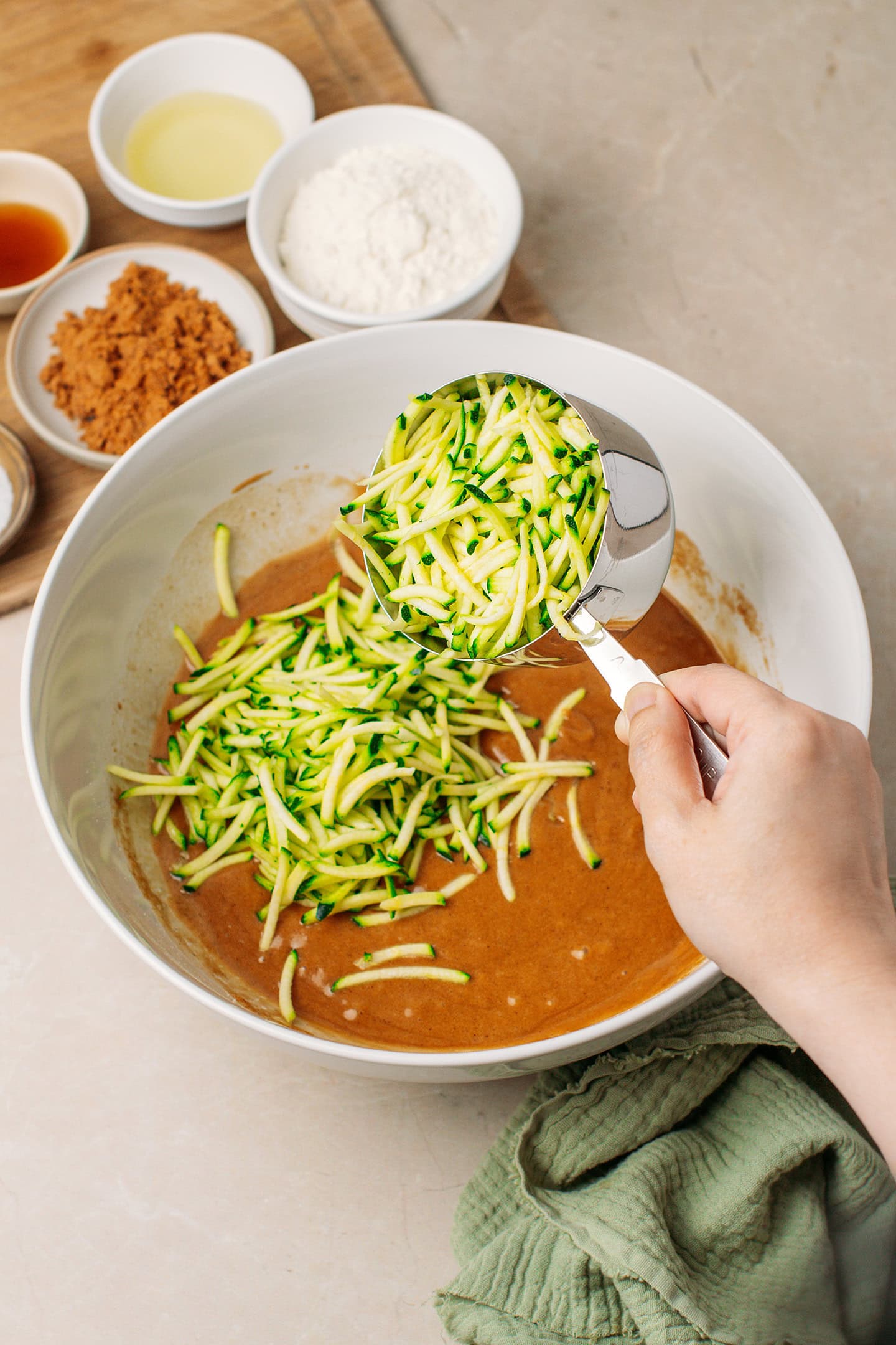 Adding a cup of grated zucchini to a mixing bowl.