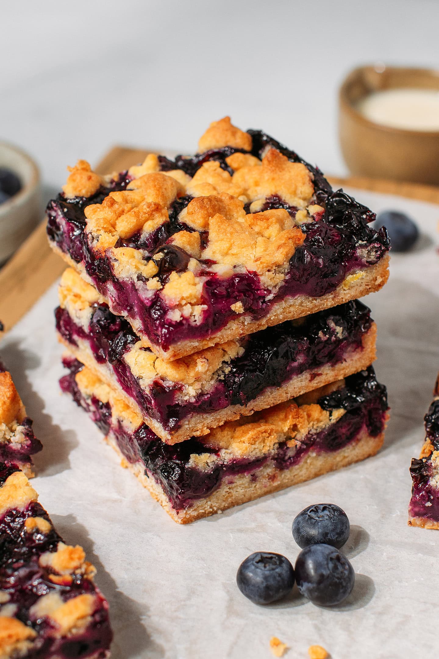 Three blueberry crumble bars stacked on a wooden board.