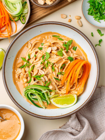 Bowl filled with peanut noodles, julienned cucumber and carrot, roasted peanuts, and chopped fresh herbs.