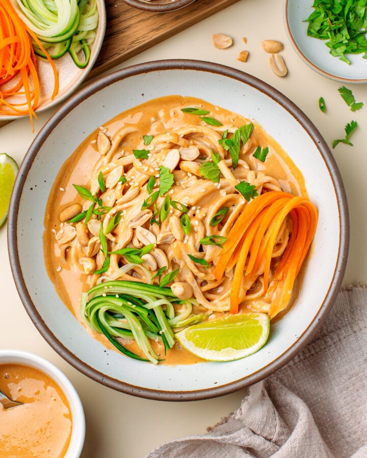 Bowl filled with peanut noodles, julienned cucumber and carrot, roasted peanuts, and chopped fresh herbs.