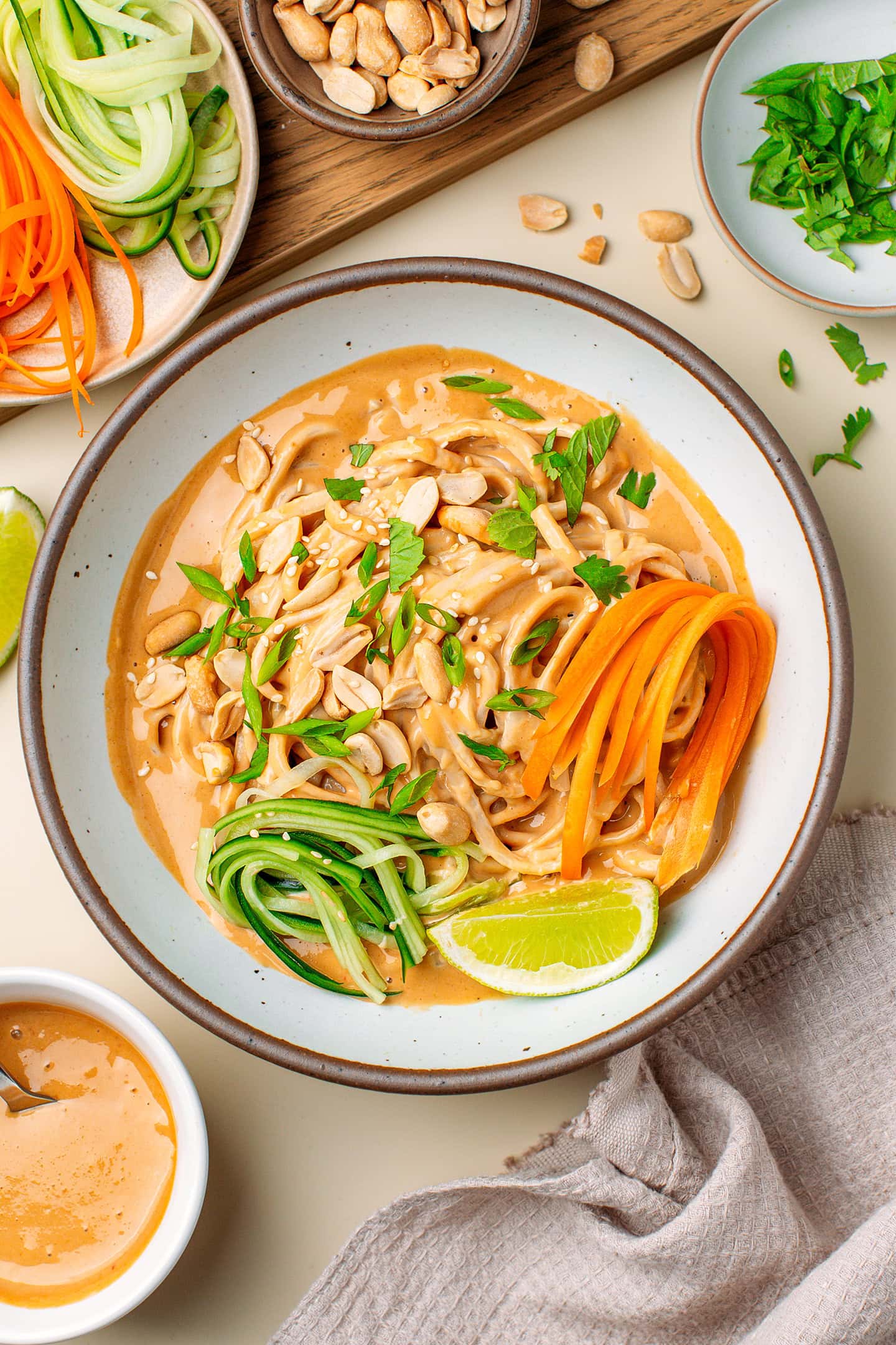 Bowl filled with peanut noodles, julienned cucumber and carrot, roasted peanuts, and chopped fresh herbs.