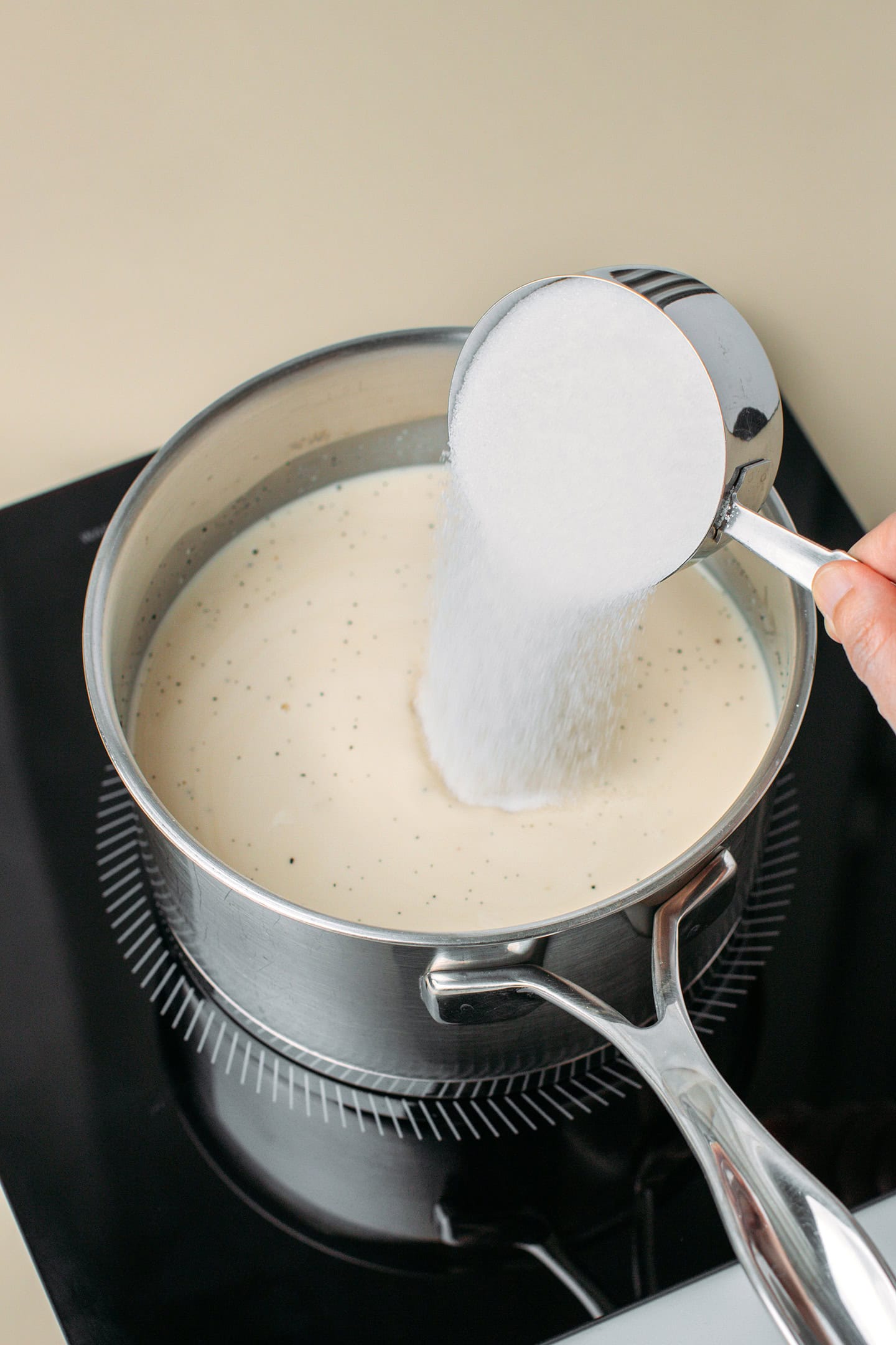 Adding sugar to a pot filled with vegan milk and cream.