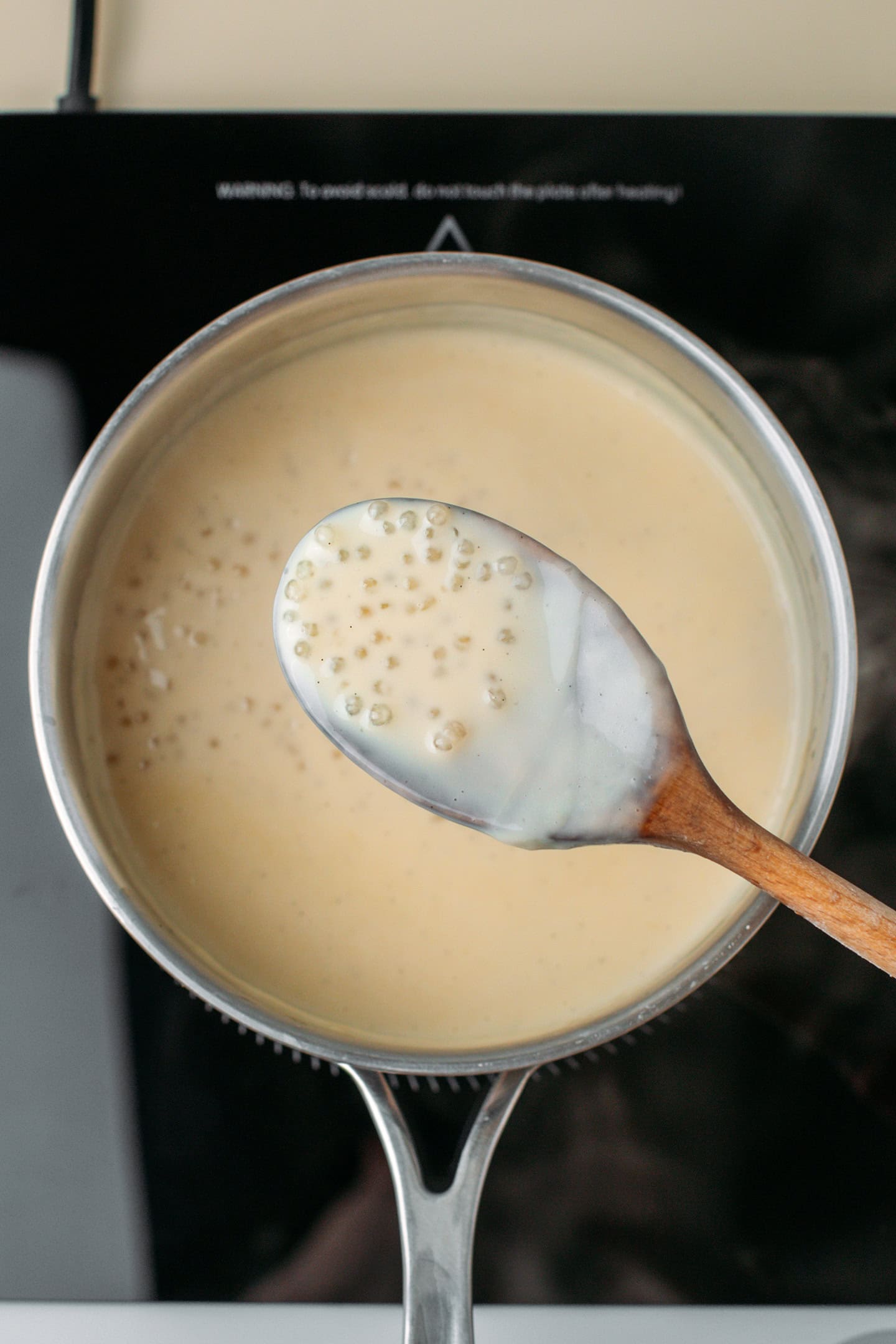 Holding a spoonful of cooked tapioca pearls over a pot.