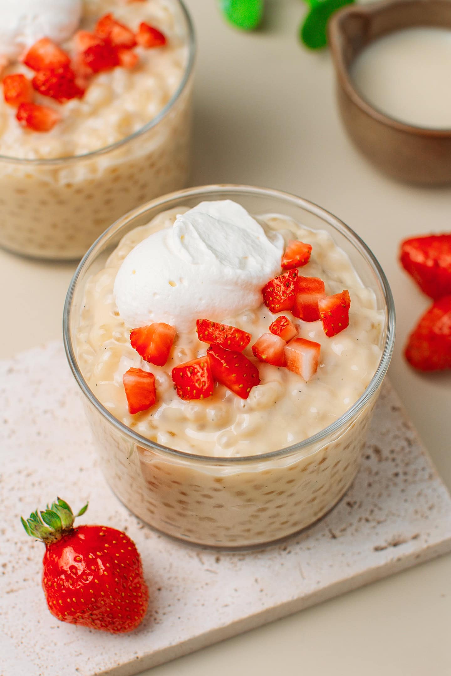 Glass ramekin filled with creamy vanilla tapioca pudding and garnished with cream and strawberries.