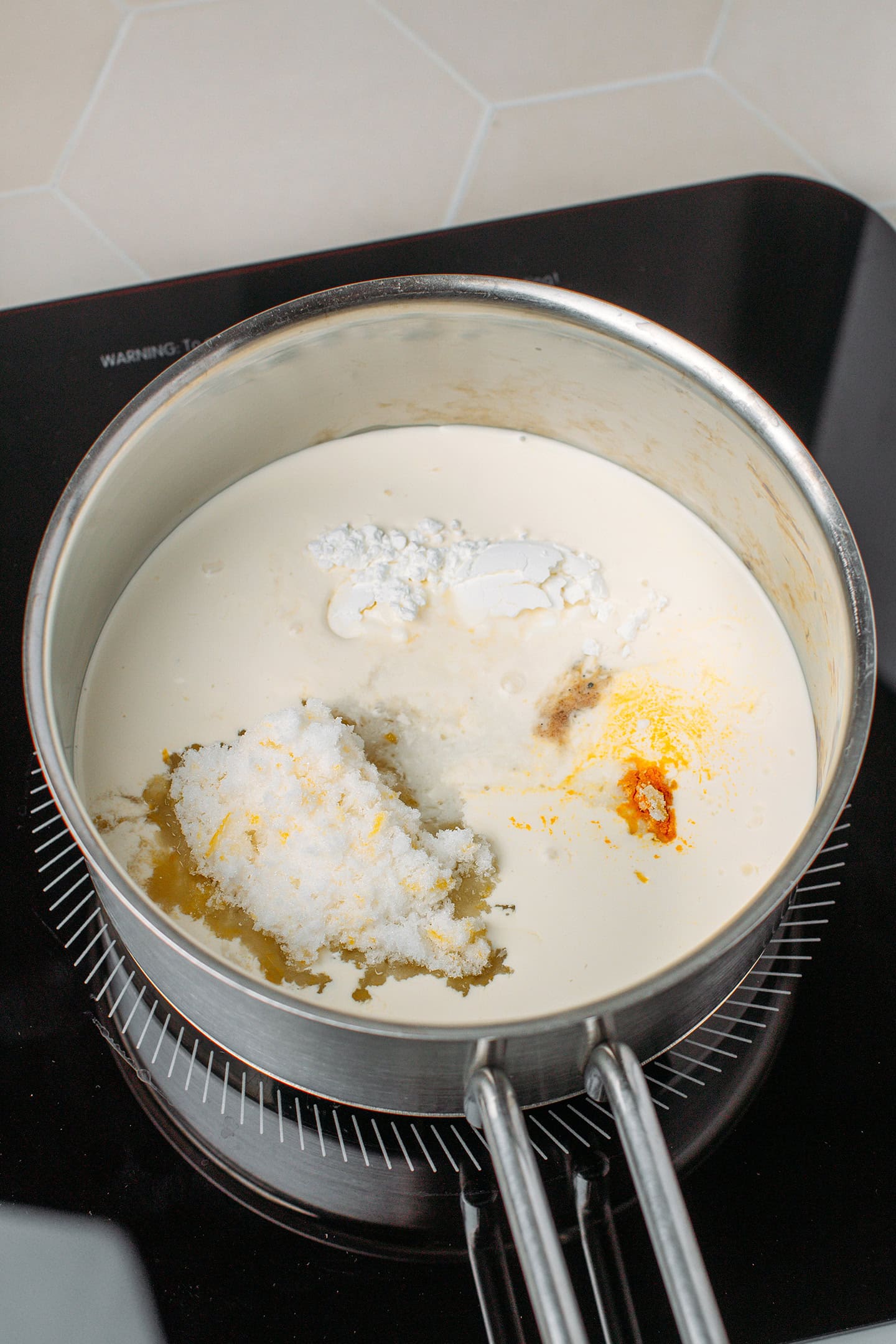 Saucepan filled with plant-based cream, sugar, turmeric, and lemon zest.