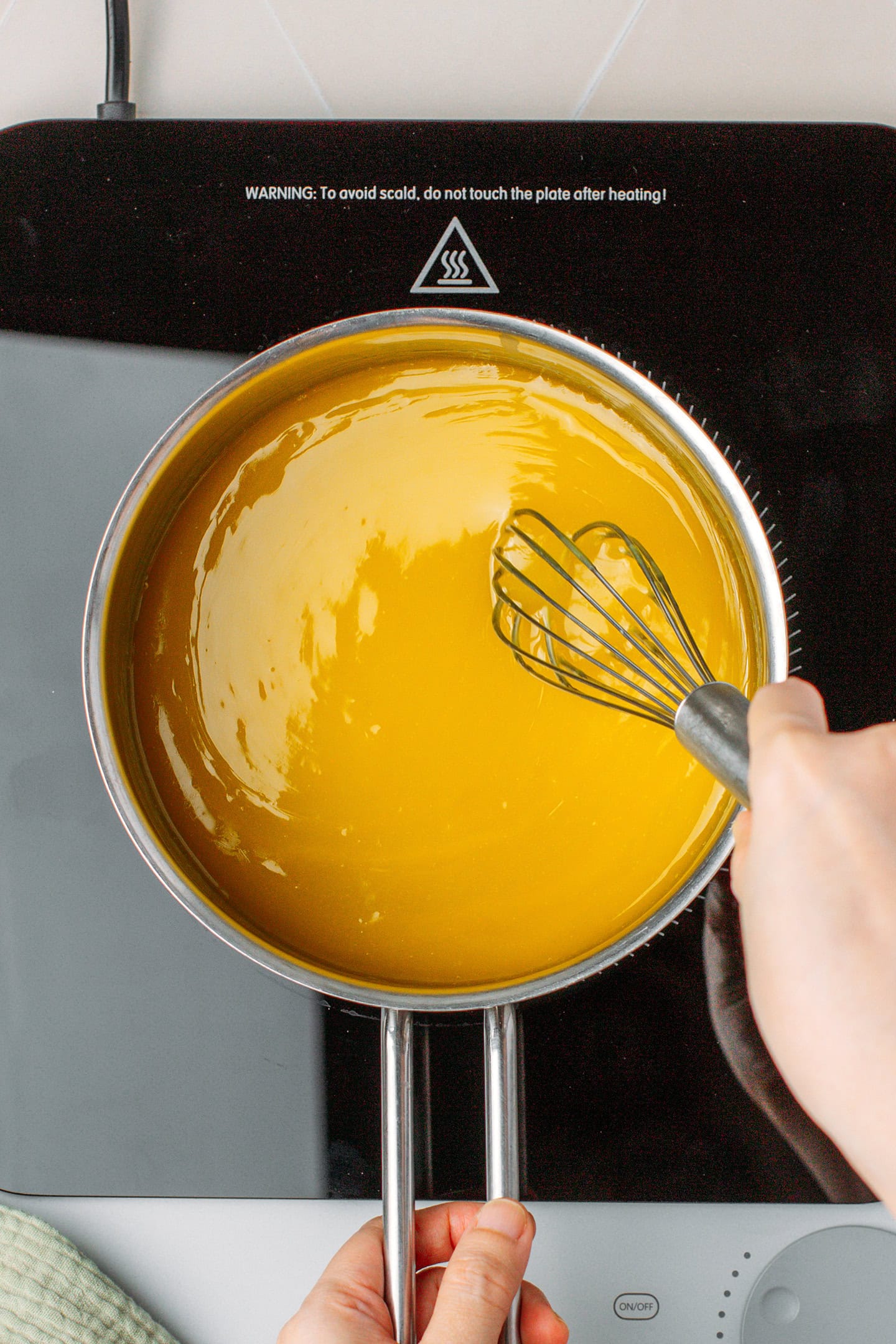 Whisking glossy lemon curd in a saucepan.