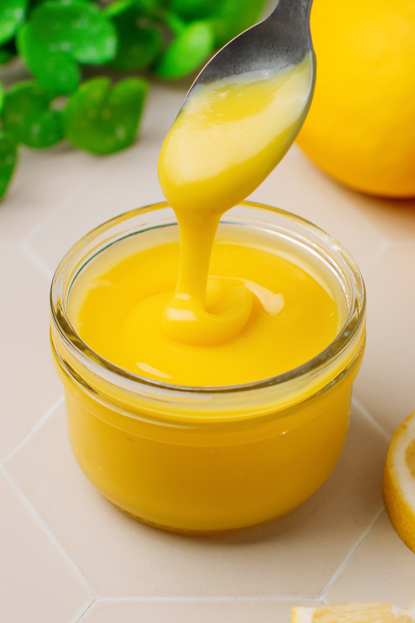Thick lemon curd dripping from a spoon into a glass jar.