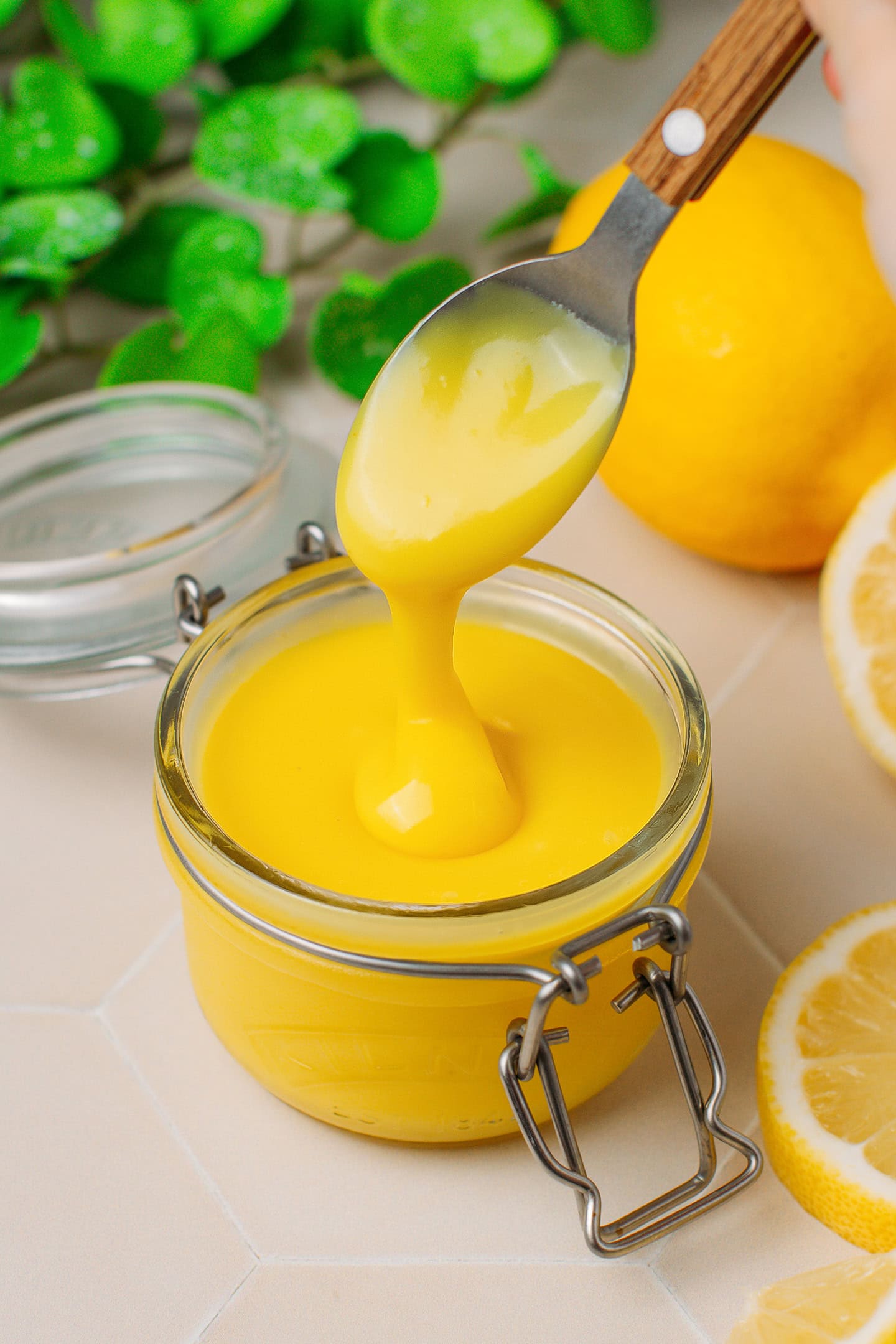 Lemon curd dripping from a spoon into a glass jar.