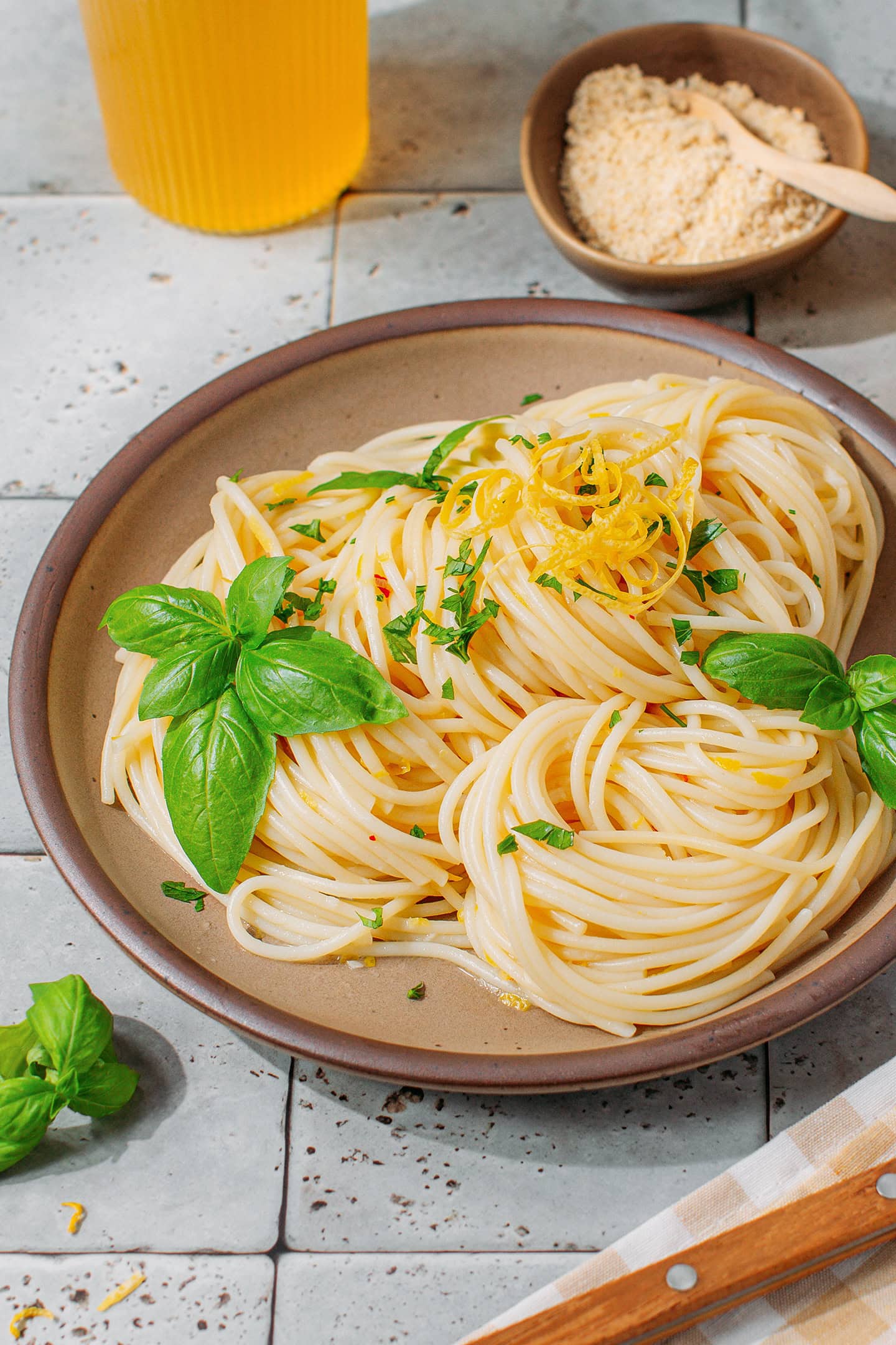 Spaghetti coated with lemon sauce and topped with fresh basil, in a brown plate.