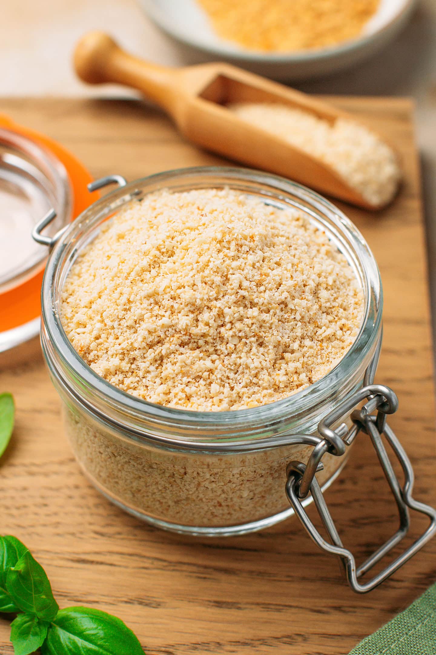 Glass jar containing vegan parmesan on a wooden board.